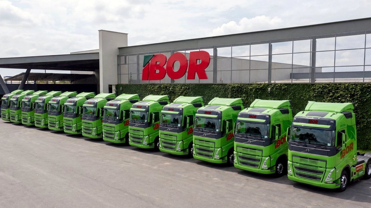 Doze caminhões Volvo FH verdes da Frota Verde IBOR enfileirados no pátio da sede.